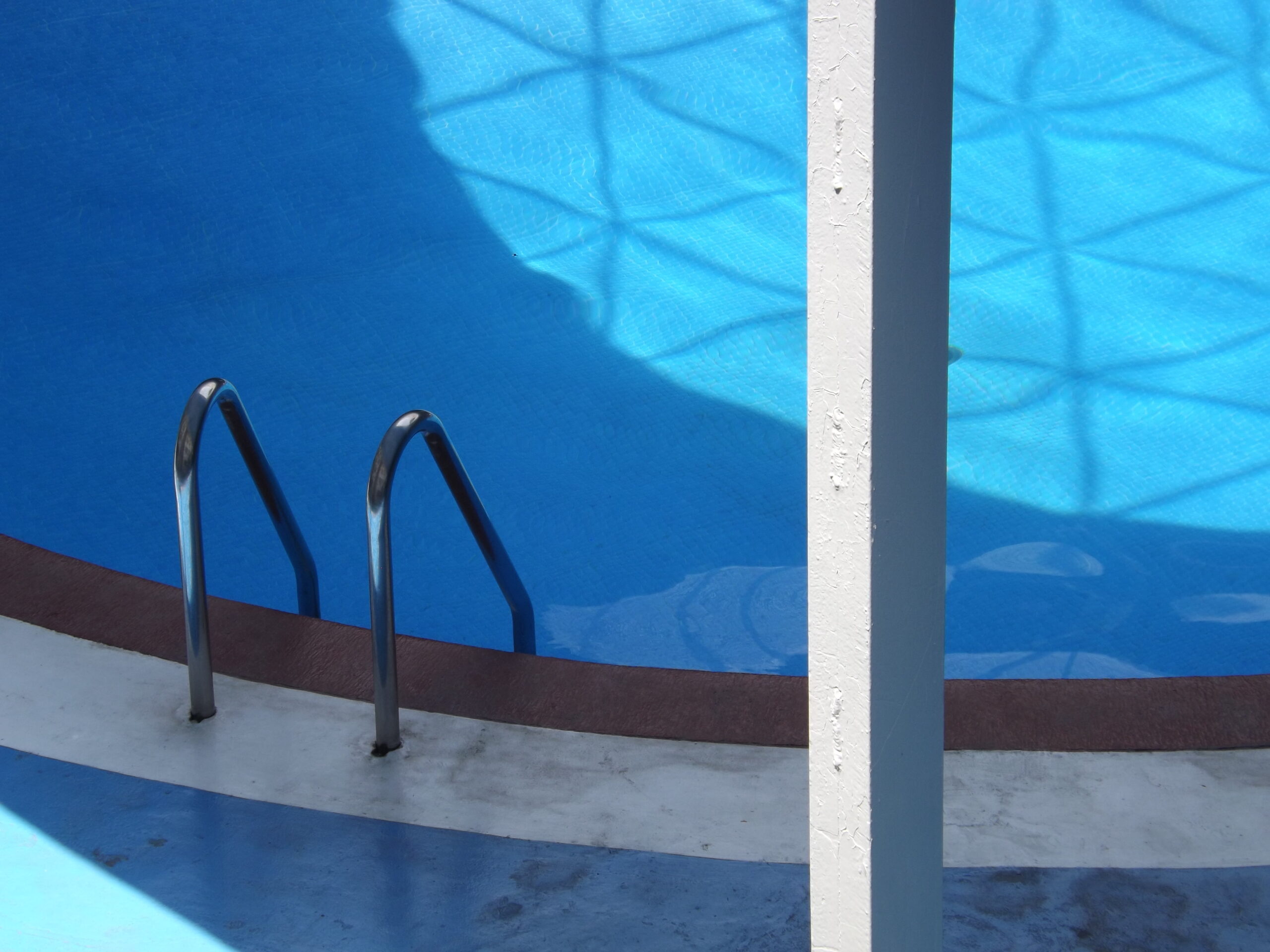 A quiet swimming pool with a metal handrail, casting shadows under bright daylight.